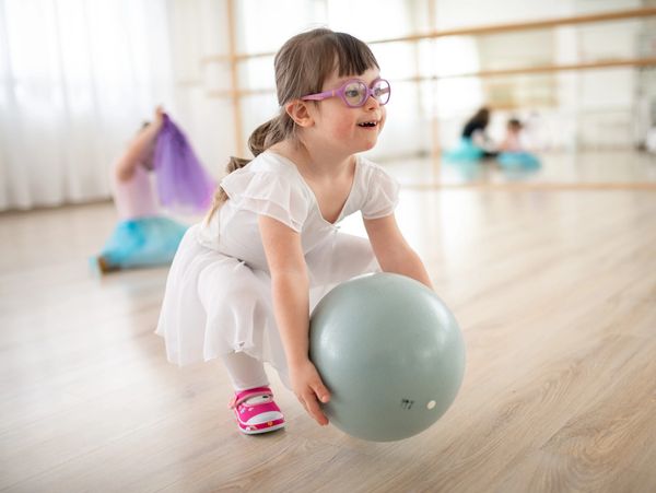 Young girl with glasses holding a ball in a dance studio.