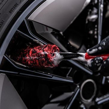 Close-up of a hand cleaning a car wheel with a soapy brush.