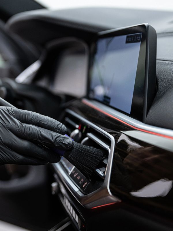 Person cleaning car dashboard vents with a brush.