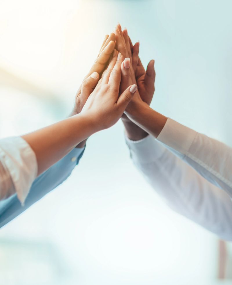 Multiracial group of students stacked hands high-five in agreement achievement success aspiration smiling in bright business office classroom