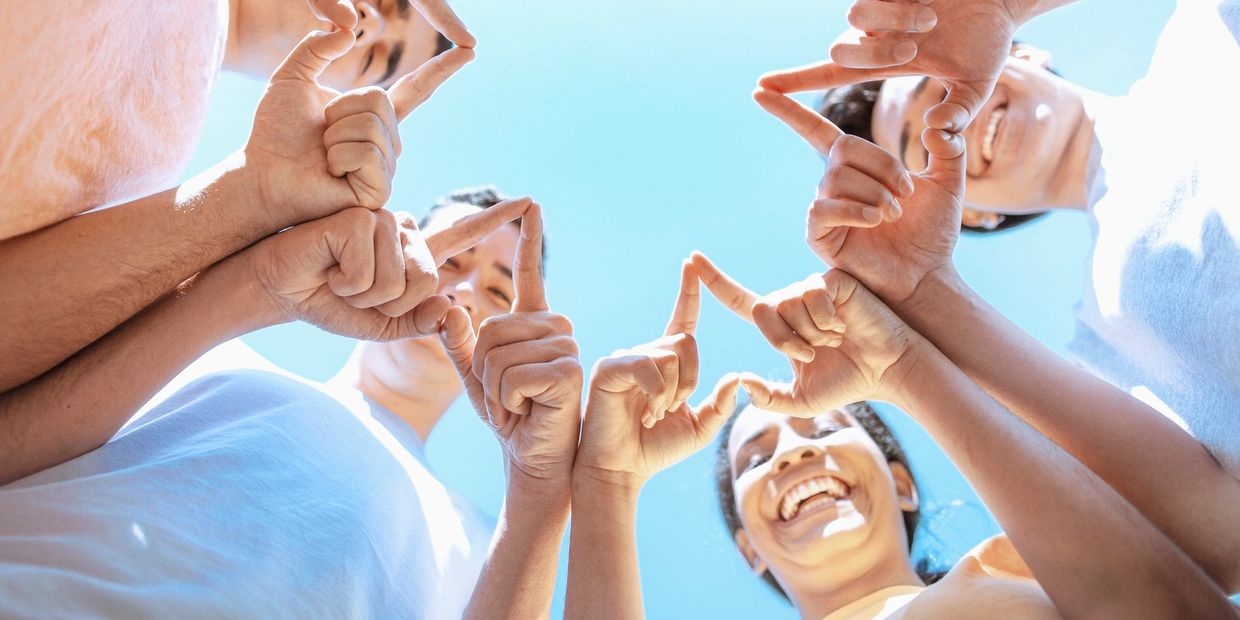Group of friends making a heart shape with their hands under a clear blue sky.