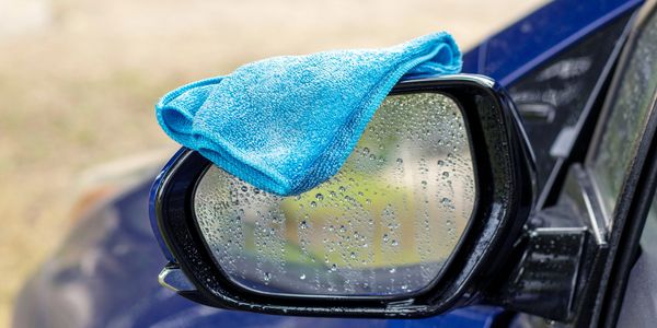 Blue cloth drying on a wet car side mirror with water drops.