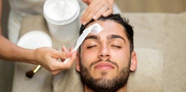 Man receiving a facial treatment with cream applied to his forehead.