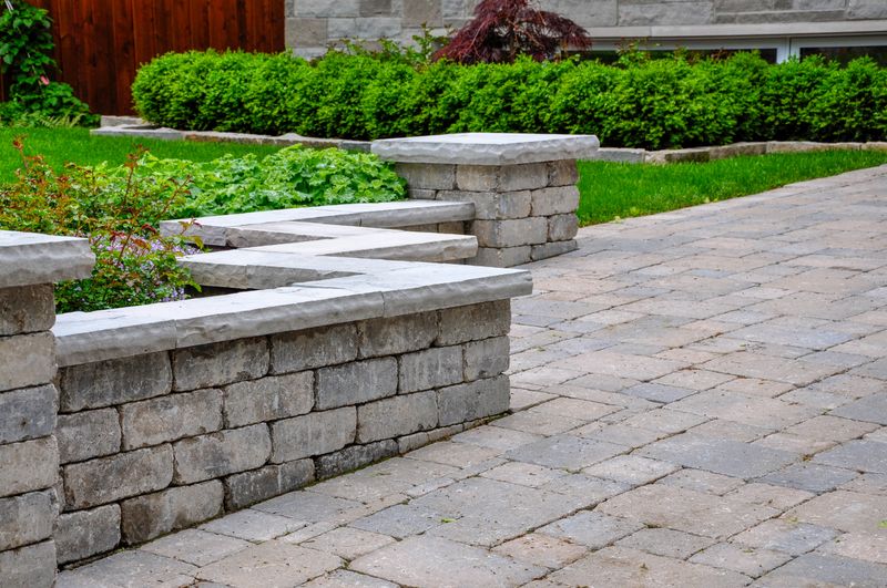 Detail of a retaining wall with pillars and natural stone coping that defines a tumbled paver driveway, creating a beautiful luxury landscaping feature.