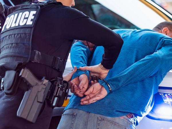 Police officers handcuffing a man in a blue shirt near a police car.