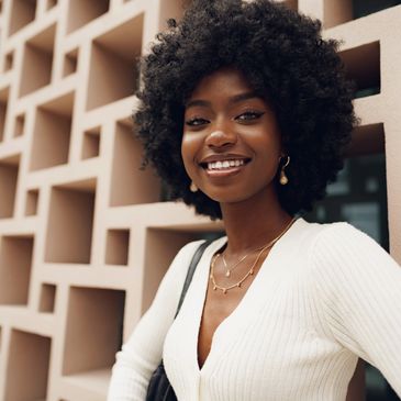 Smiling woman with natural curly hair wearing a white top and gold jewelry.