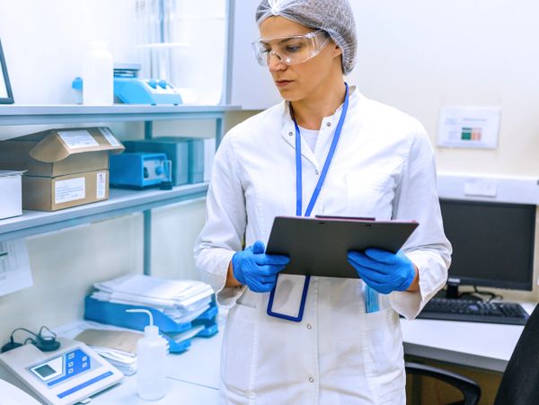 Scientist in lab coat and gloves reviewing clipboard in laboratory.