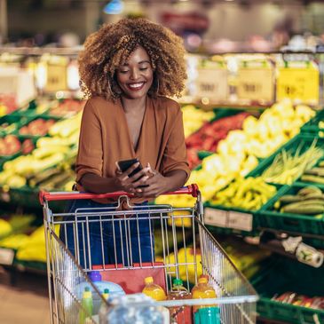 Smiling woman shopping with a cart, using her phone.