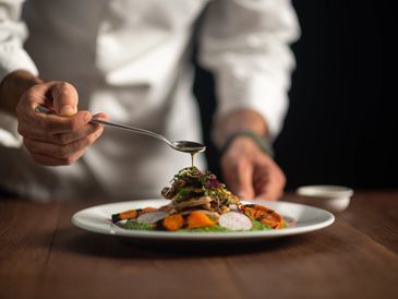 Chef adding sauce to plated gourmet dish.