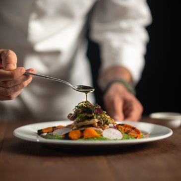 Chef drizzling sauce on a gourmet plated dish.