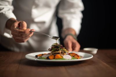 Chef garnishing a plated dish with sauce.
