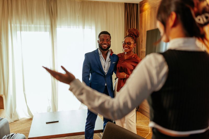 A female concierge is in an apartment suite with wealthy hotel guests showing them their luxurious apartment suite.