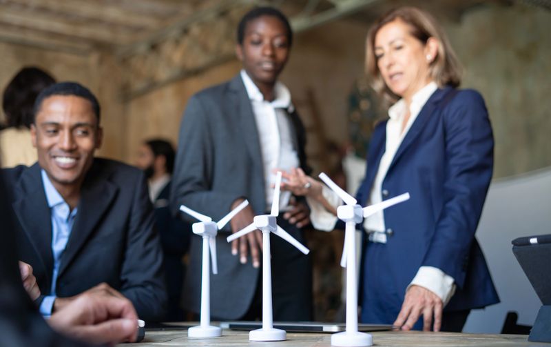 Business portrait of engineers team discussing about a wind power plant project.  Models of a wind turbine on the table. Ecology theme and new sustainable energy concept