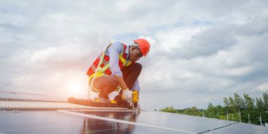 A worker installs solar panels on a roof with safety gear.