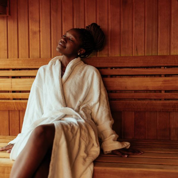 Woman relaxing in a sauna wearing a white robe.
