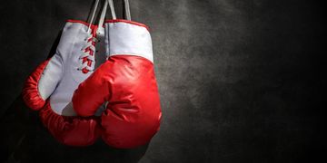 Red boxing gloves hanging on a dark wall.