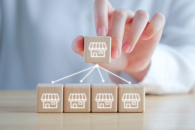 Franchise Business marketing concept. Hand holding franchise store icon on wooden blocks with line network connection to another store.