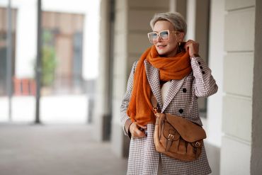 Stylish woman in sunglasses and orange scarf outdoors.