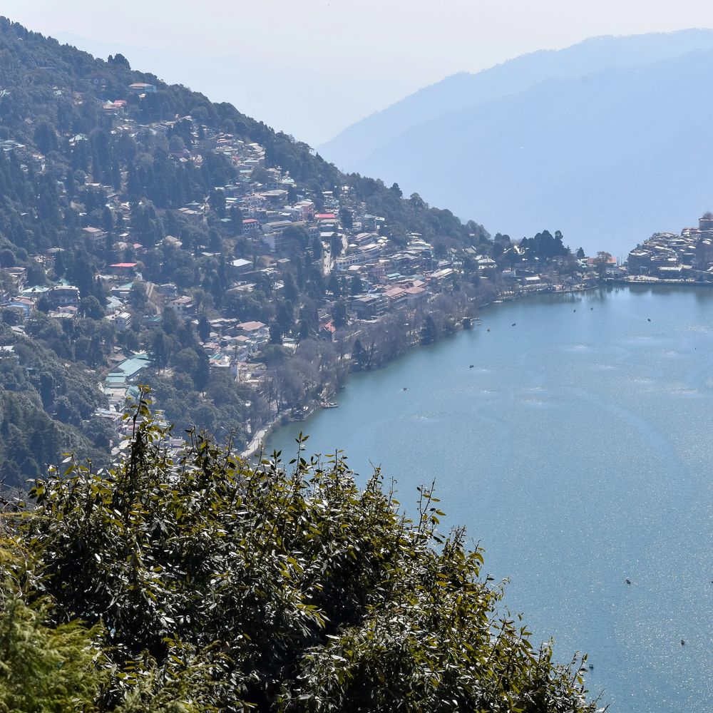 Scenic view of a lakeside town nestled among forested hills under a hazy sky.