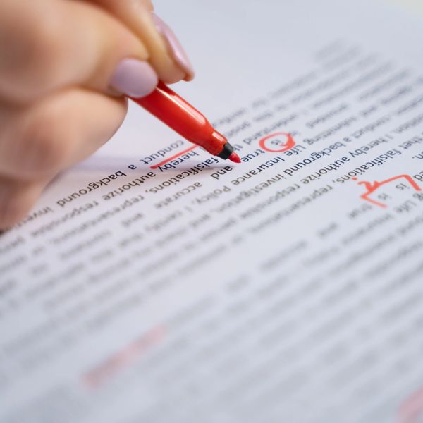 Hand editing a document with a red pen, marking corrections and underlining text.
