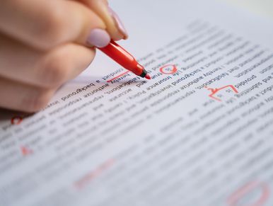 Hand editing a document with a red pen, marking corrections and underlining text.