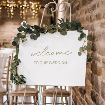 Elegant wedding welcome sign adorned with greenery on an easel.