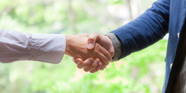 Two people shaking hands in a business setting outdoors.