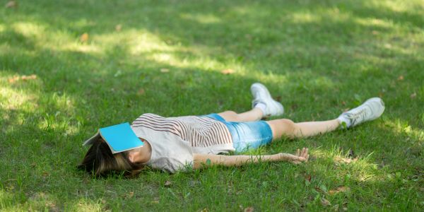 Person lying on grass with a book on their face.