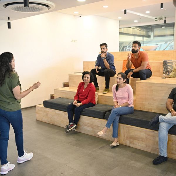 A woman speaks to a small seated group in a modern office setting.