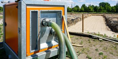 A large orange water pump with connected hoses at a sandy construction site.
