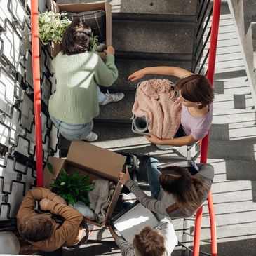 Five people carrying boxes and belongings up a stairwell, likely moving in or out.
