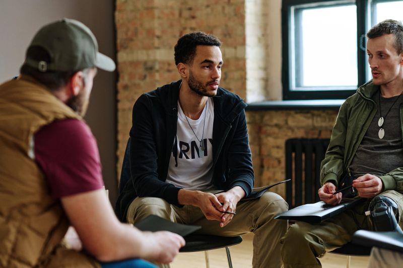 A group of Black men sitting on a couch, engaged in deep conversation about mental health.