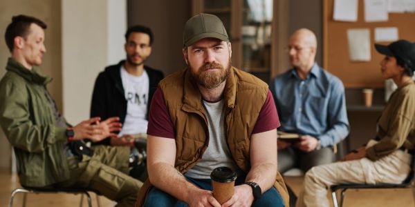 Man with coffee cup sits in front of group discussion.