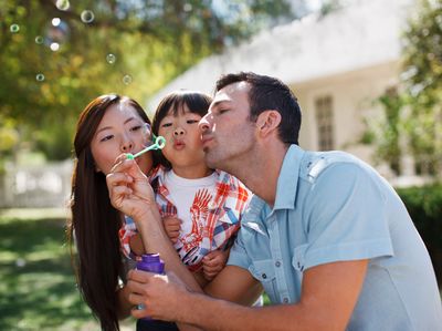 Family blowing bubbles together outdoors on a sunny day.