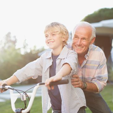 Grandfather teaching grandson to ride a bike on a sunny day.