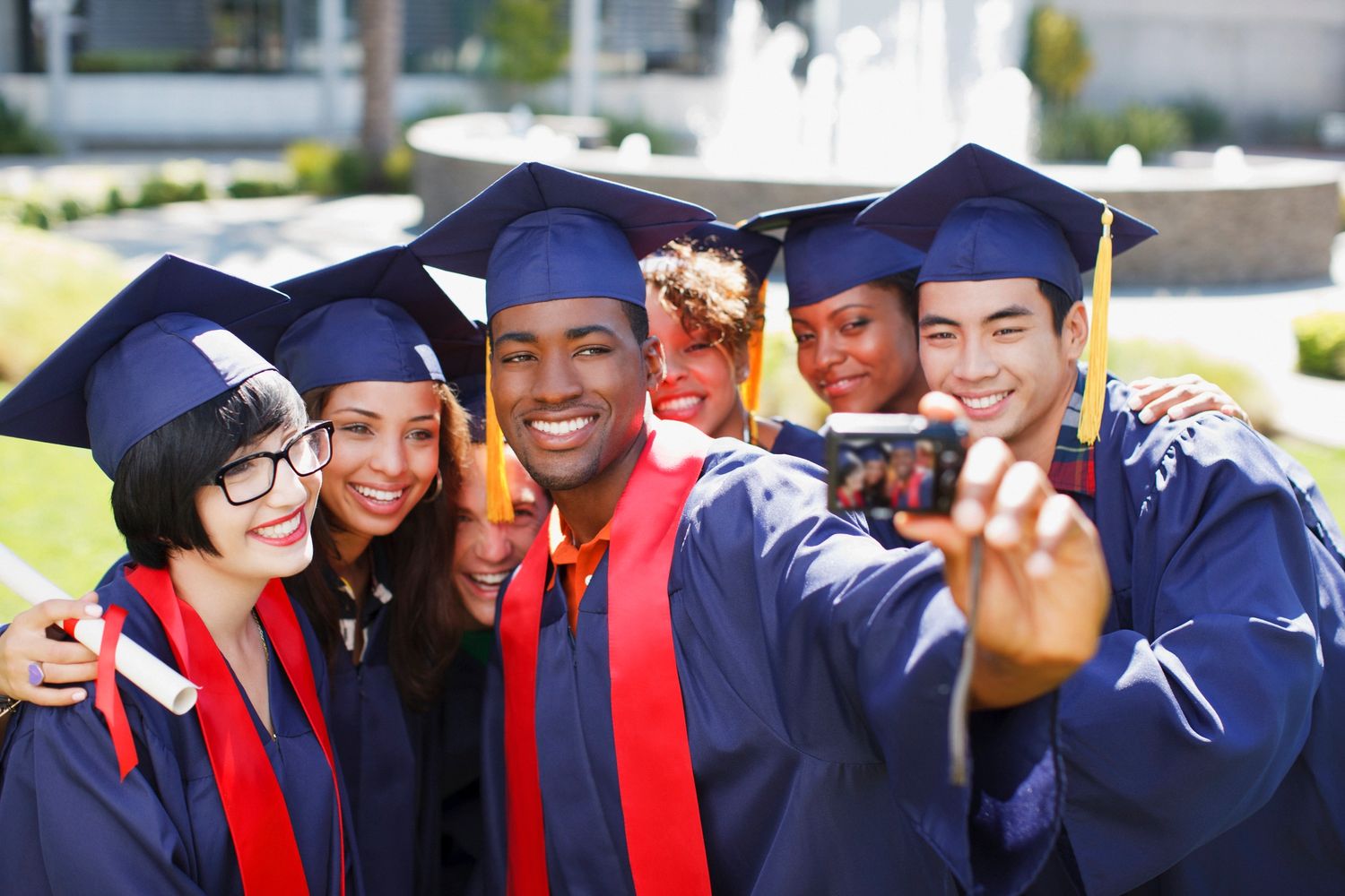 A group of diverse graduates in caps and gowns taking a selfie outdoors.