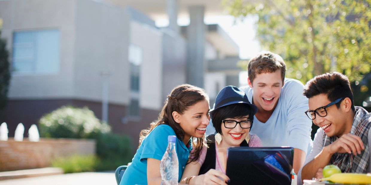 Group of friends happily looking at a tablet outdoors.