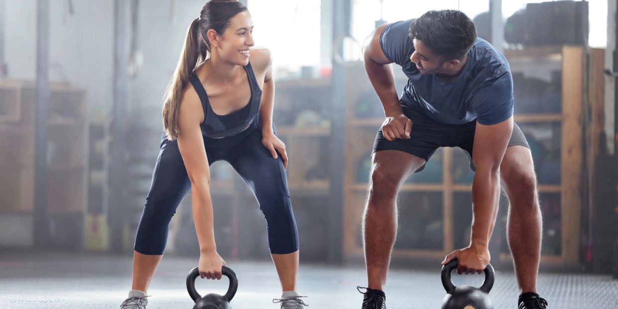 Two people exercising with kettlebells while smiling at each other.