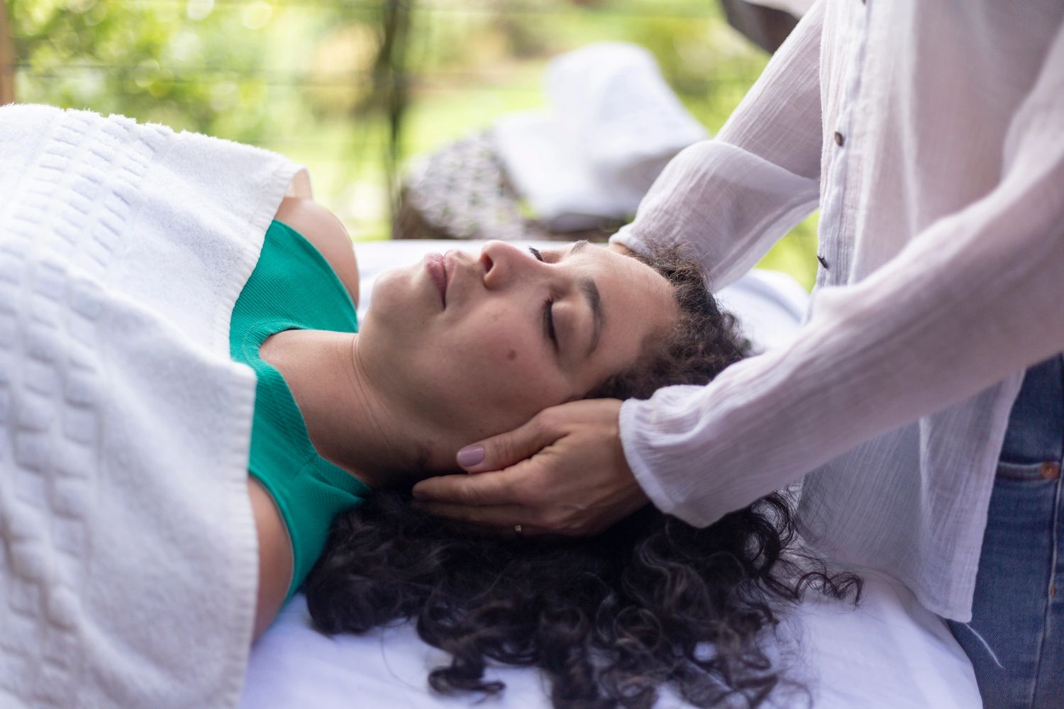 A woman receiving a relaxing head massage outdoors.