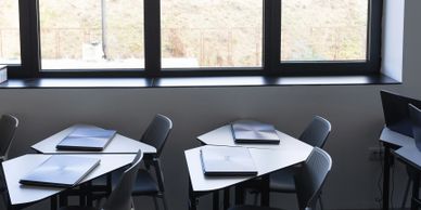 Empty classroom with laptops on desks near a window.