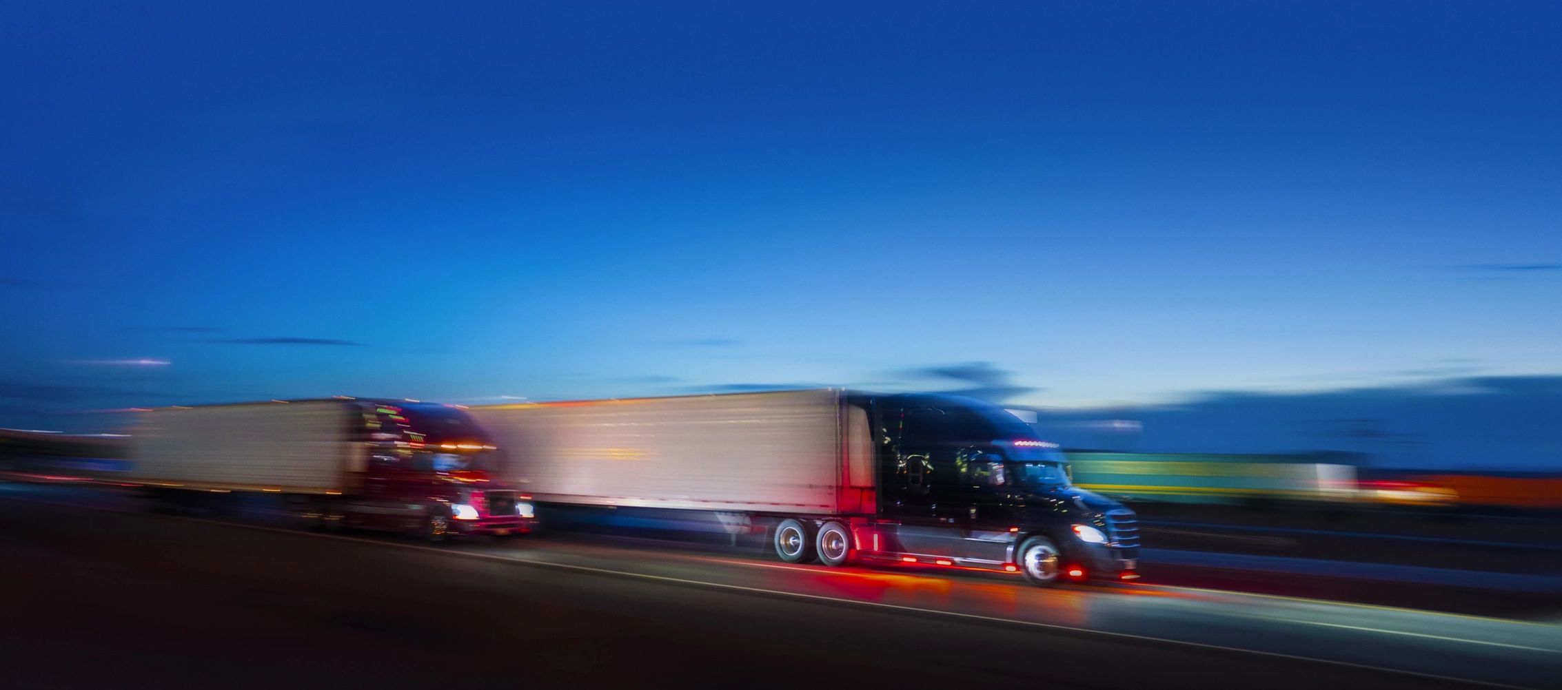 Two semi-trucks driving fast at dusk.
