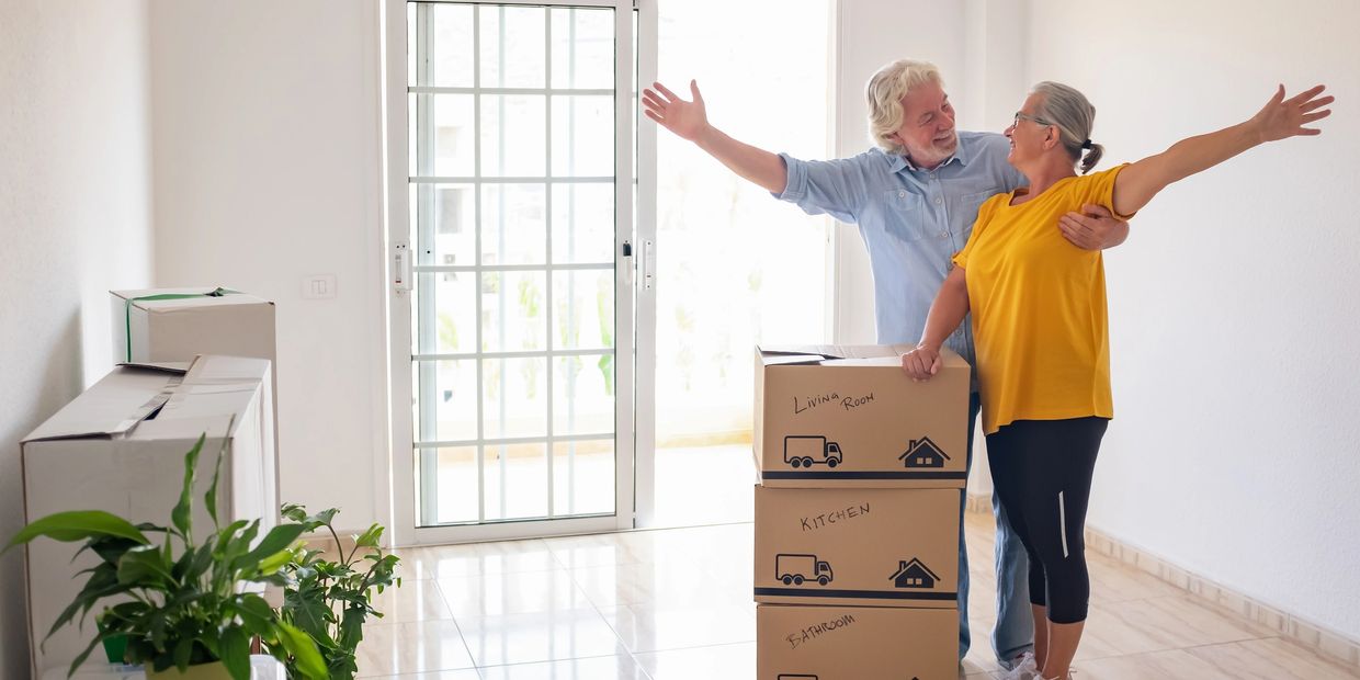 A joyful elderly couple stands with moving boxes in their new home.