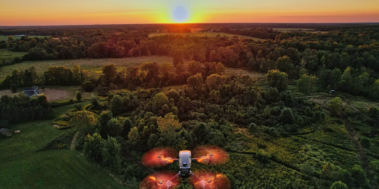 A drone flying over a lush forest at sunset with glowing propellers.