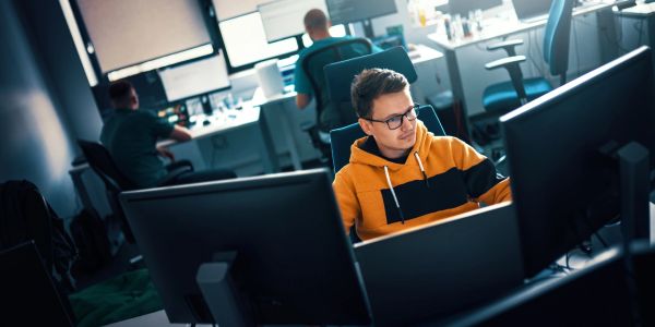 Young man working on a computer in an office with multiple monitors.
