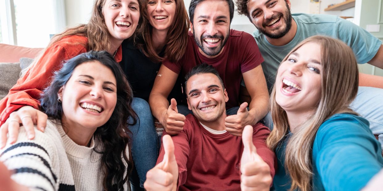 Group of friends smiling and giving thumbs up selfie.