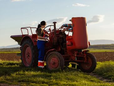 Person operating a red tractor in a field.