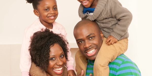 Happy family with parents carrying their smiling children on their shoulders indoors.