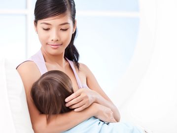 A mother breastfeeding her child indoors.