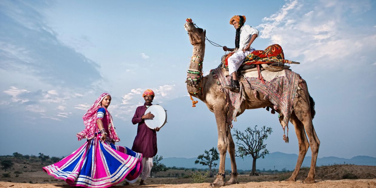 Traditionally dressed people with a camel in a desert setting.