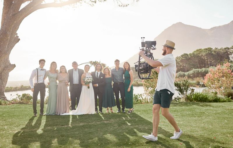 Wedding, photography or videography with family portrait at outdoor lake park or natural event. Group of people for together marriage with professional videographer and video camera or photographer